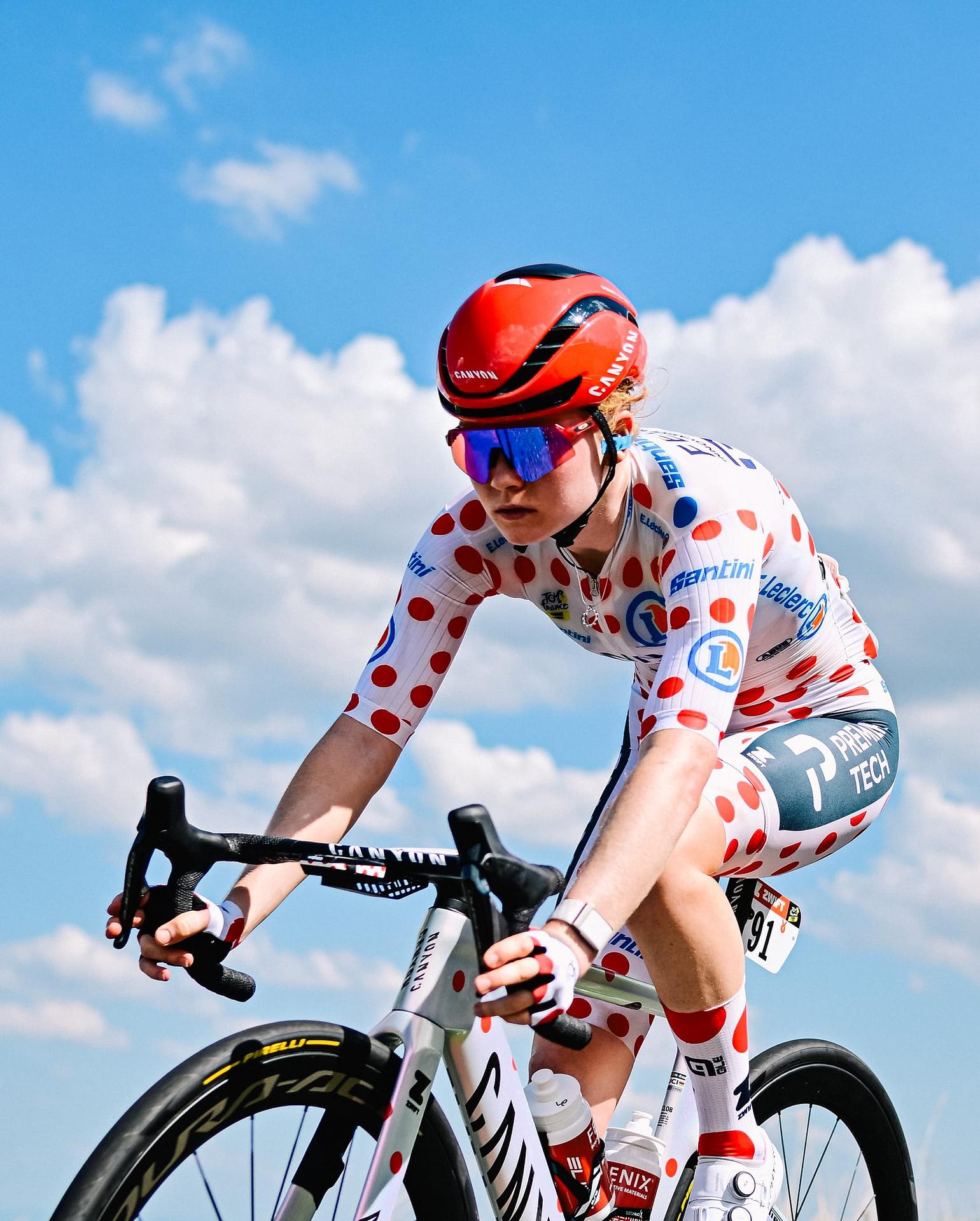 Cyclist in polka-dot racing kit leans into the ride on a bike against a bright blue sky
