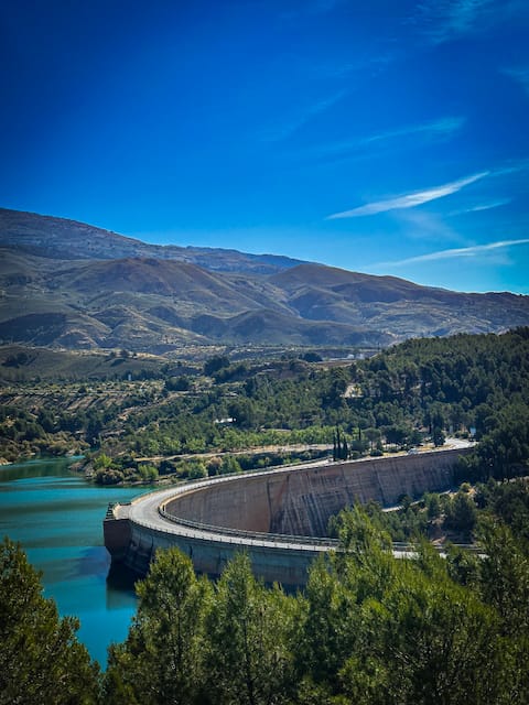 Turquoise mountain reservoir bordered by a sweeping concrete dam and forested hills