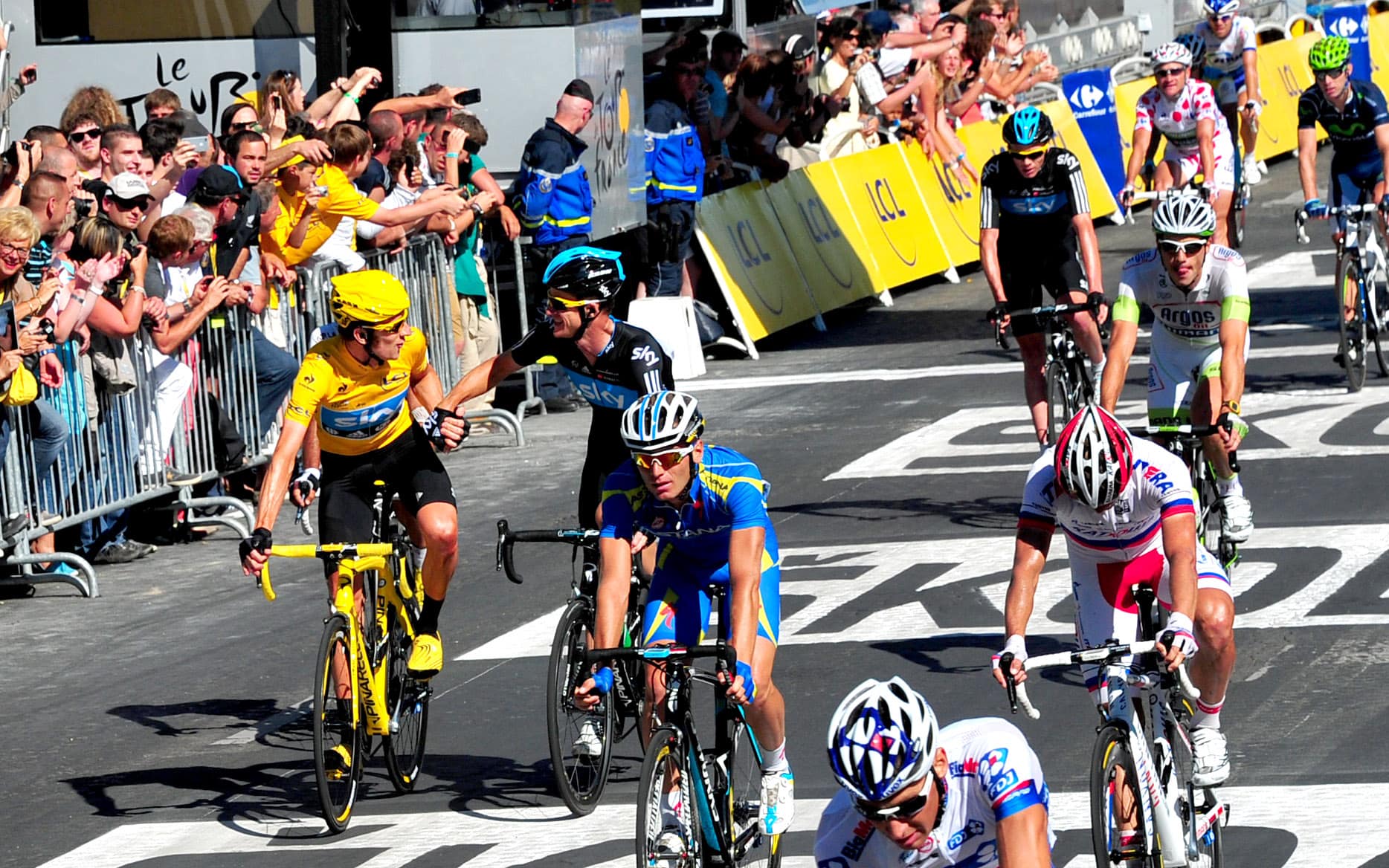 Tour de France riders in a sprint along the Champs-Élysées as fans cheer behind barriers
