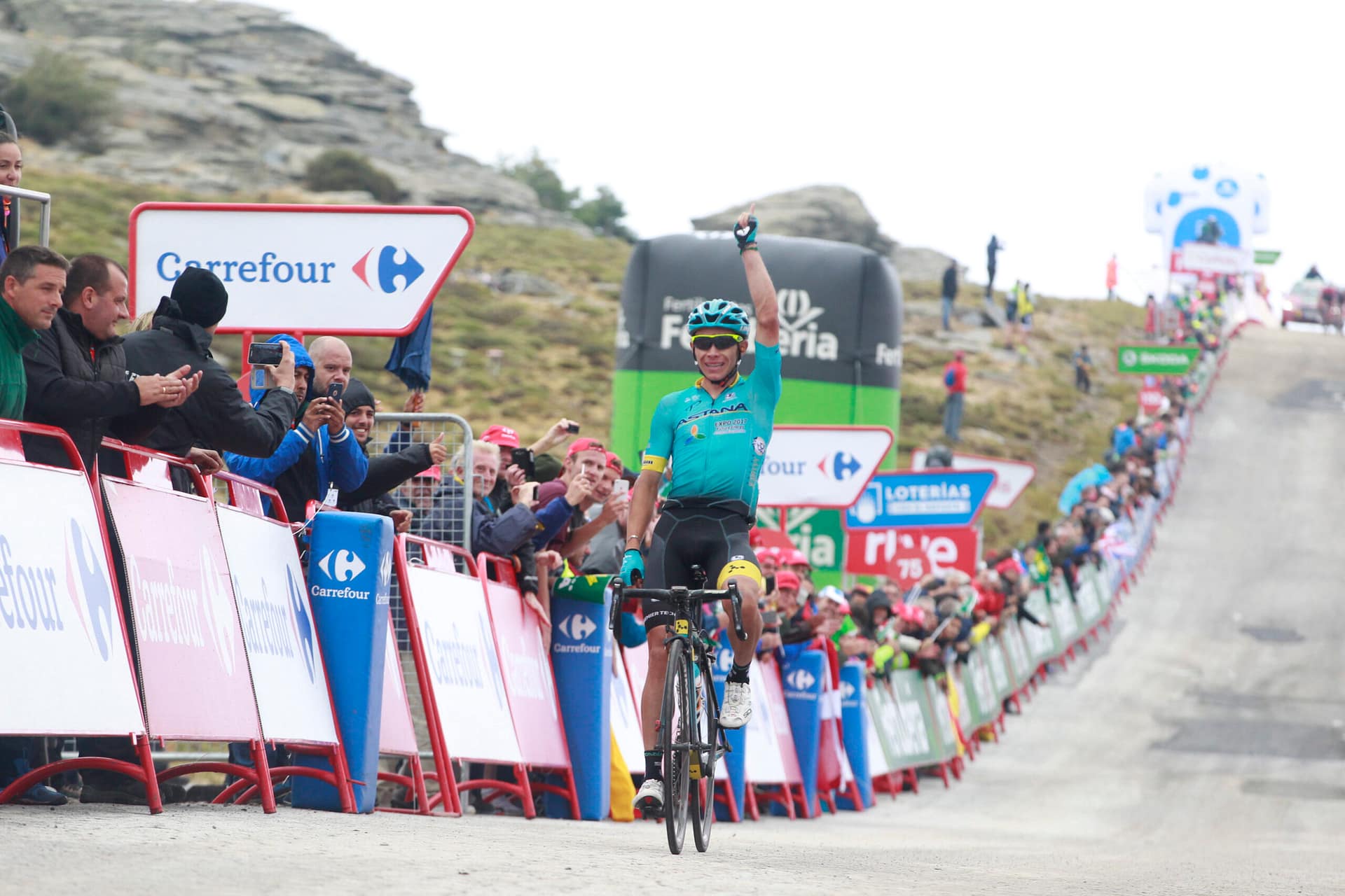 Cyclist climbs a steep mountain road past cheering fans and Carrefour barriers