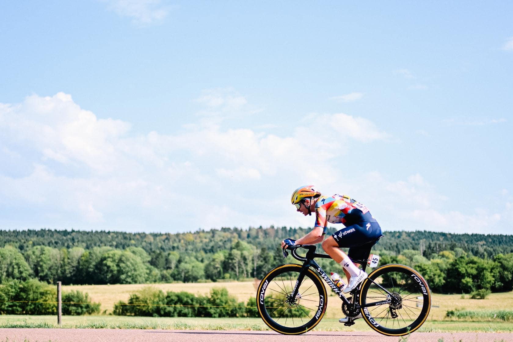 Cyclist in colorful kit rides fast on a road bicycle during an open-country sprint.