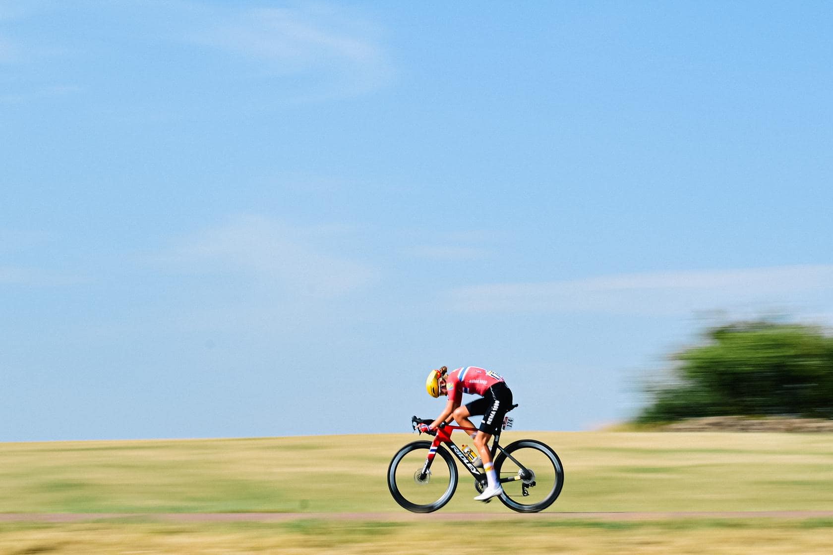 Cyclist in colorful kit speeds along a countryside road during daytime, leaning into a turn.