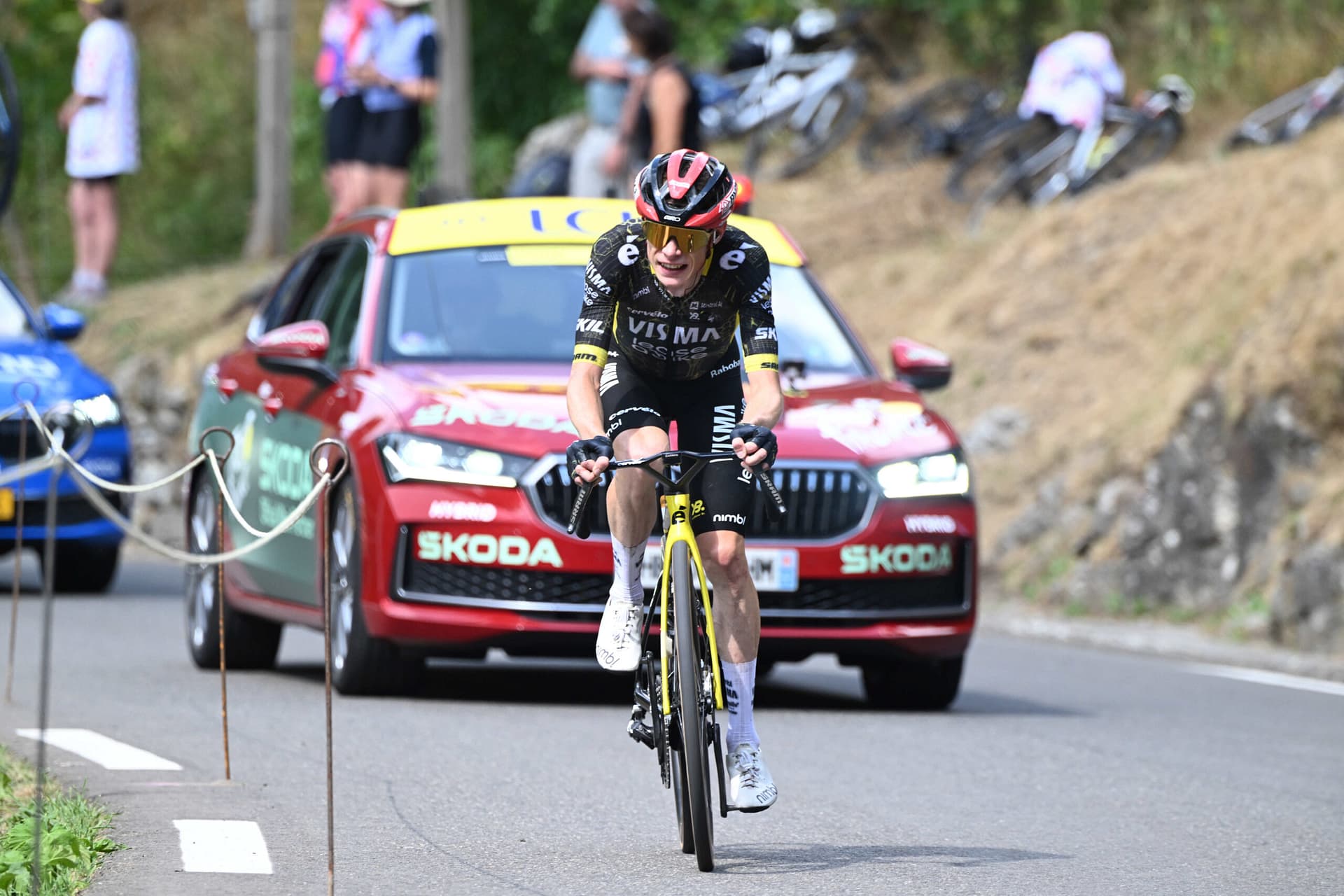 Cyclist sprints uphill in a road race as race cars follow on a mountain road