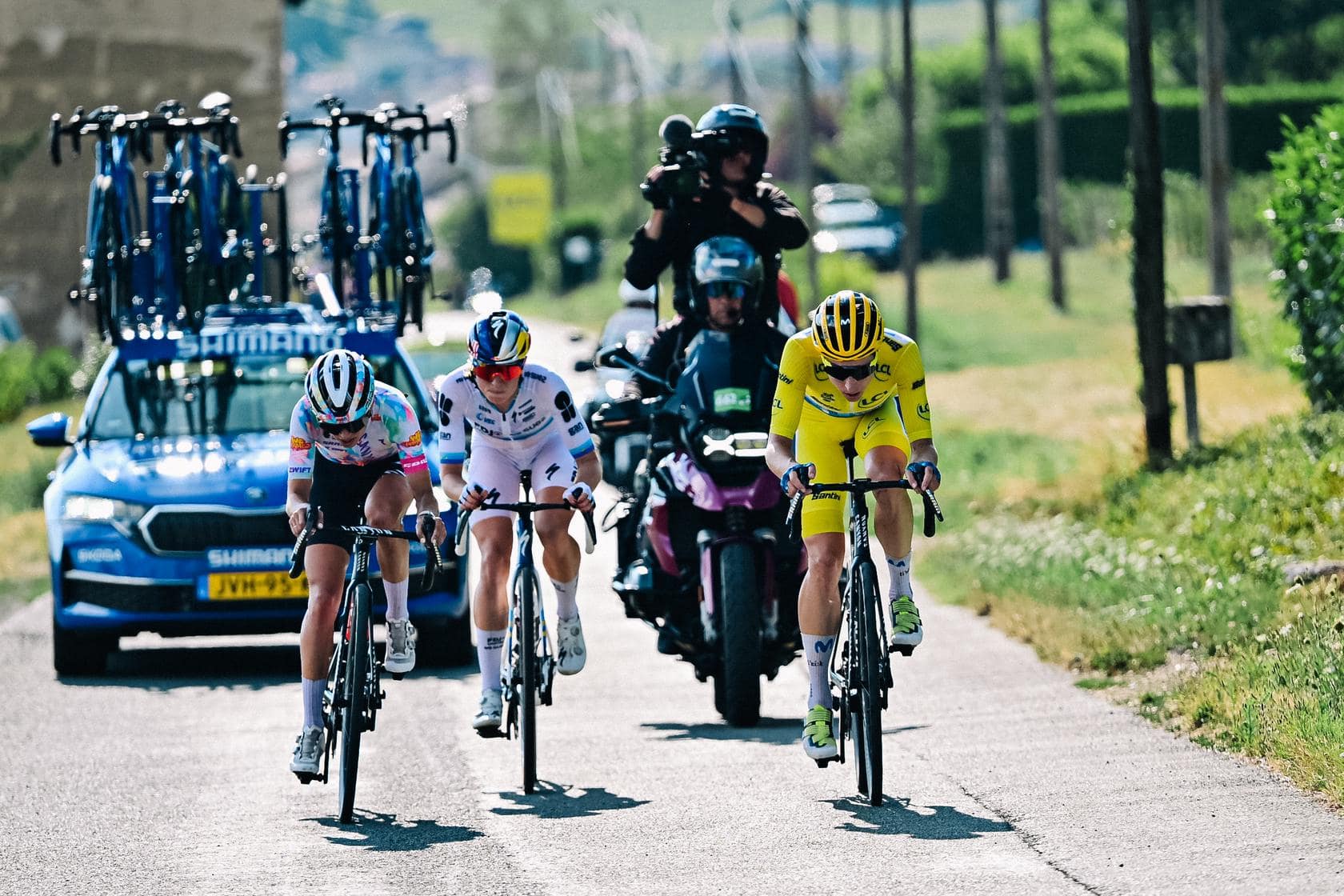 Road cyclists sprint in a group with vehicles following during a Tour de France-style race