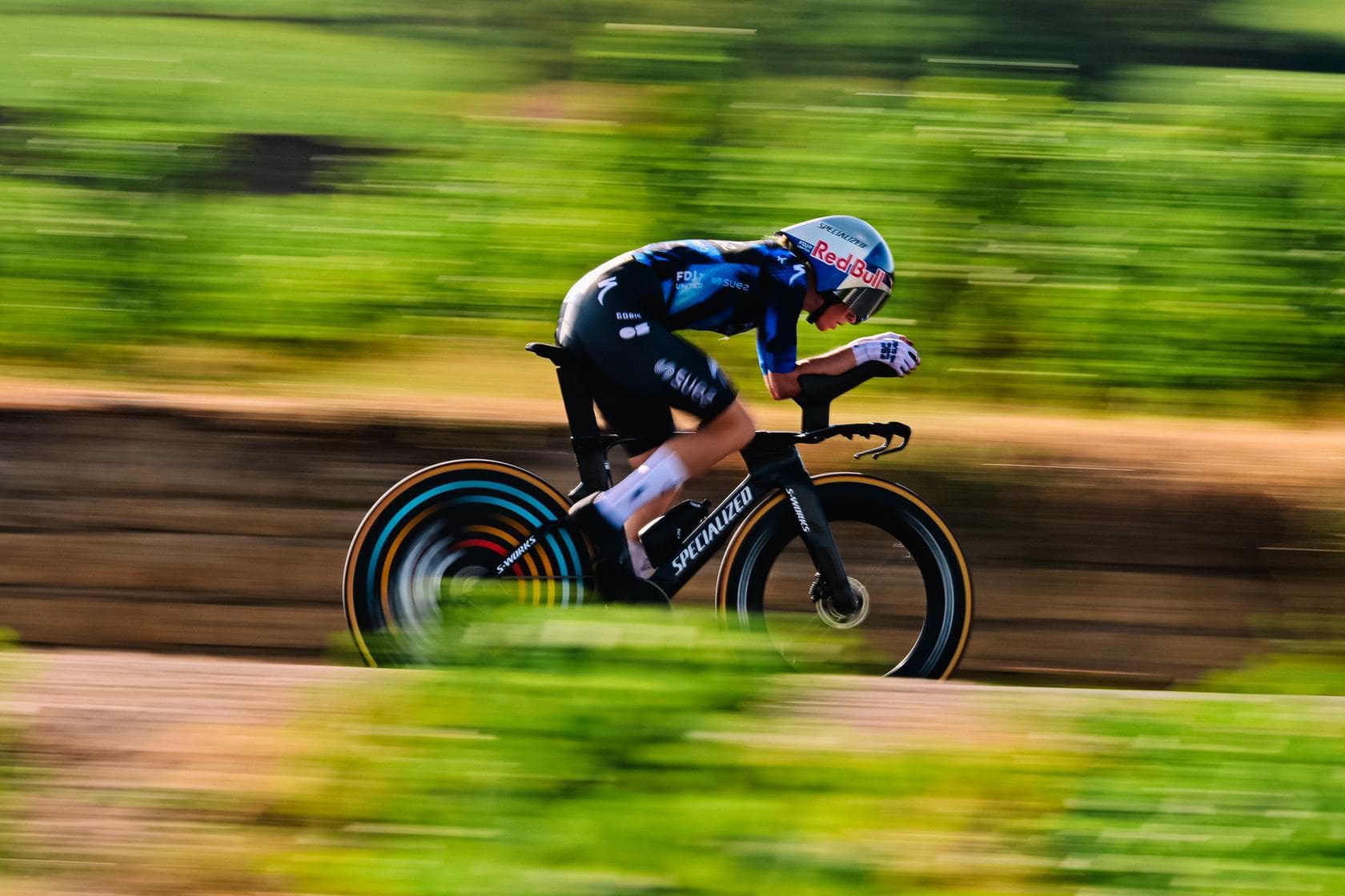 Cyclist in blue and black kit races downhill on a road bike during a Tour-style event sprint.