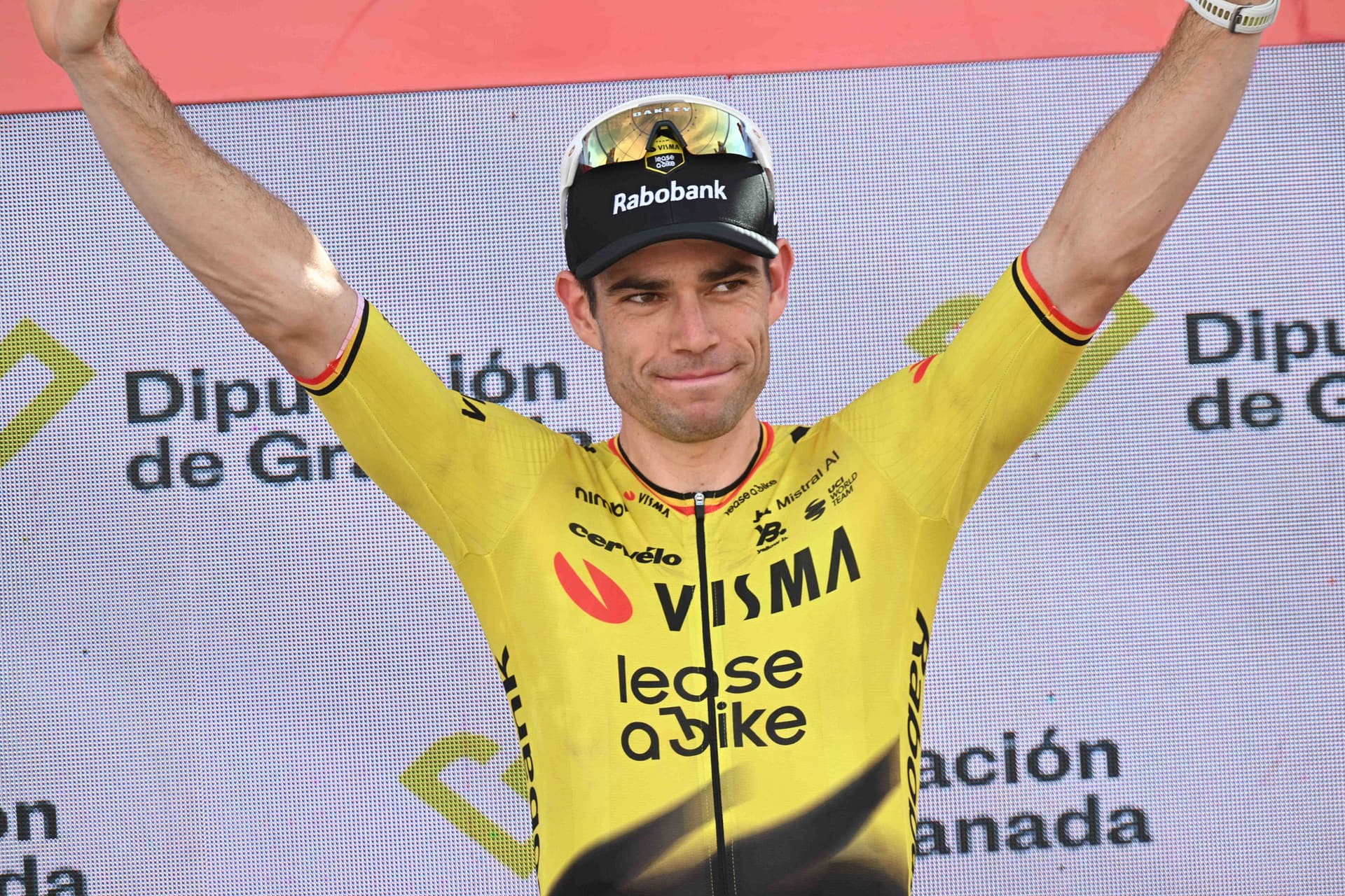 Wout van Aert viert zijn Vuelta-zege op het podium met beide armen omhoog in zijn gele Visma-shirt.