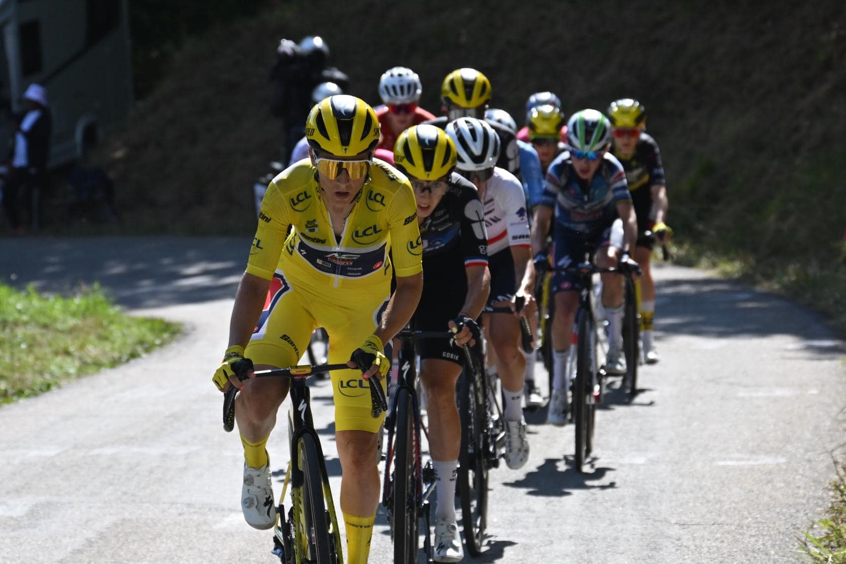 Cyclists in yellow jerseys ride in a road race, leading a group up a mountain road.