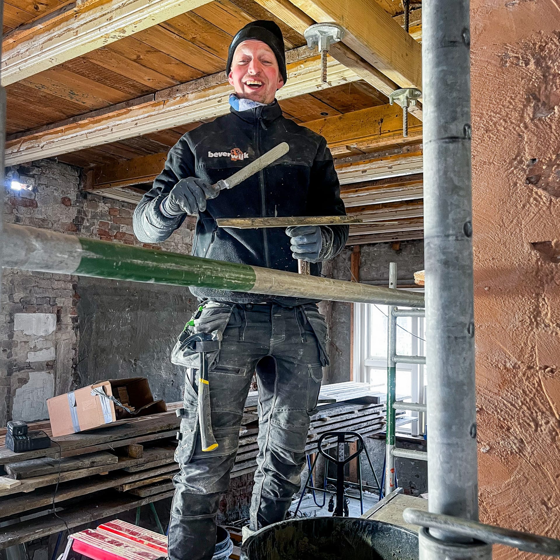 Medewerker van WerkKragt is aan het werk op de bouw en is aan het metselen met een wintermuts op en een lach op zijn gezicht.