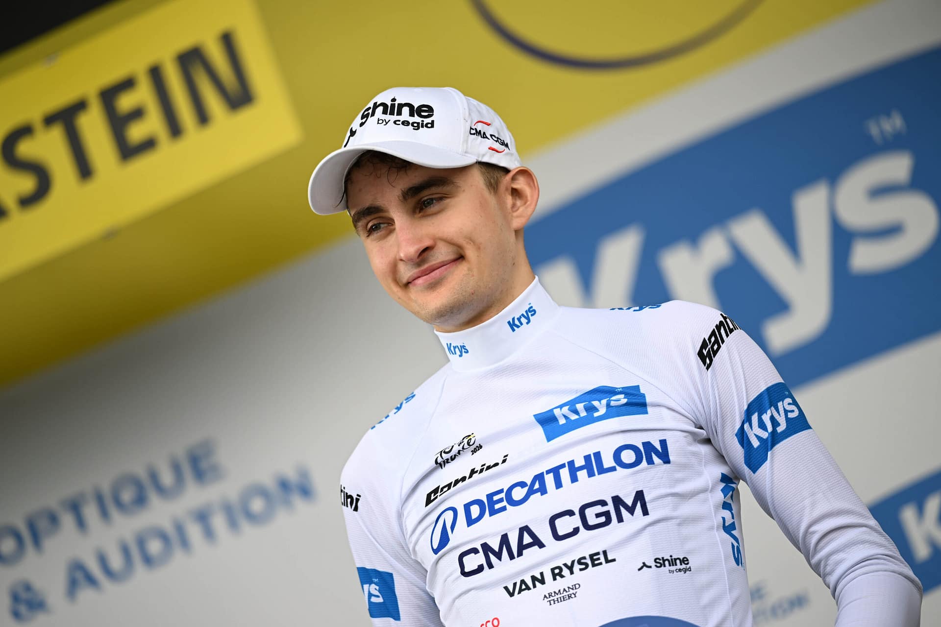 Cyclist in team kit posing outdoors near Tour de France sponsor boards