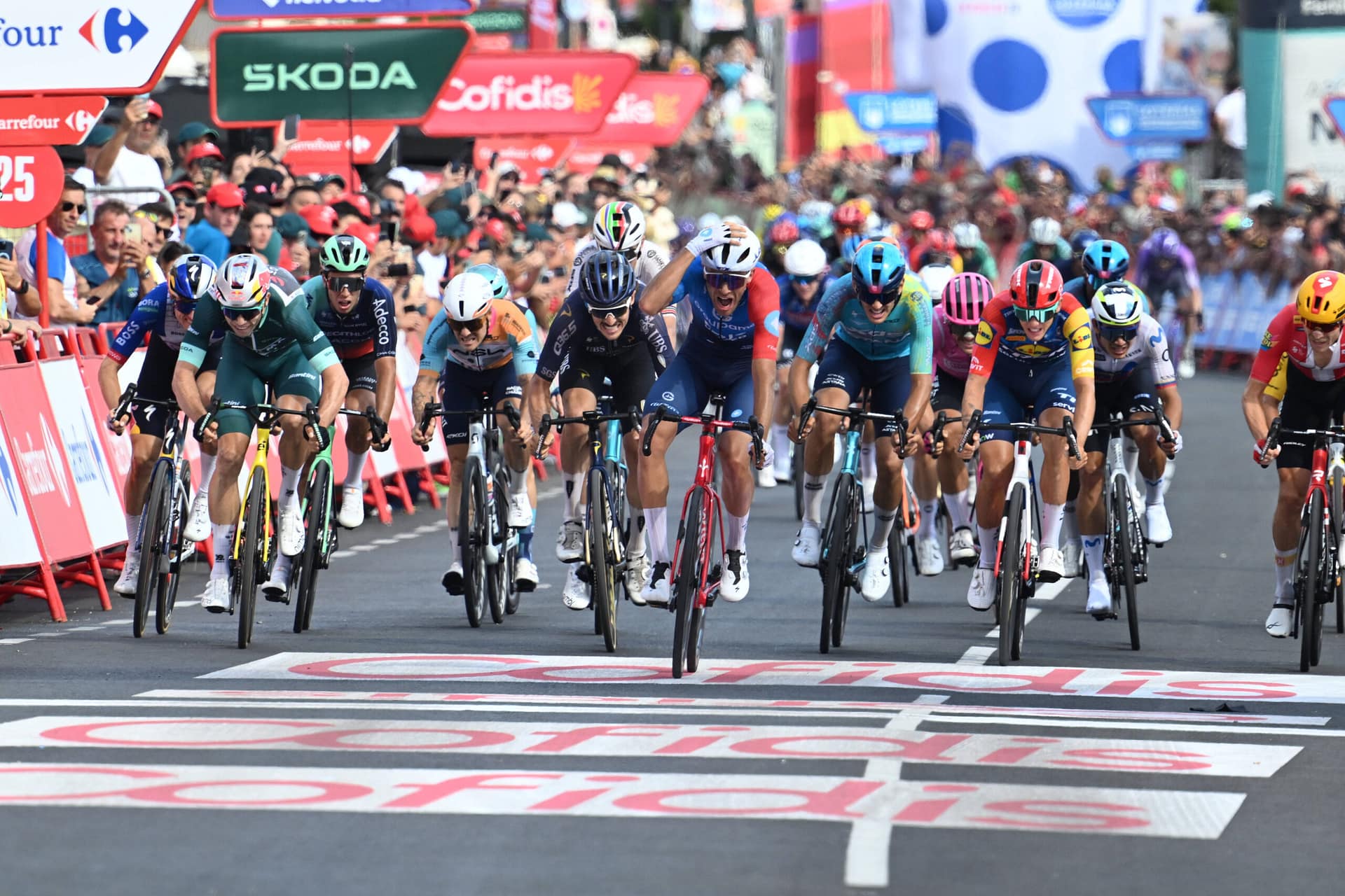 Peloton of Vuelta a España riders sprints toward the finish line in a crowded town center