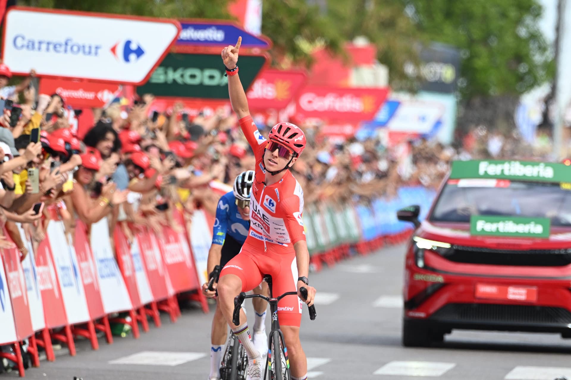 Tadej Pogačar raises a finger while riding past cheering fans at the Vuelta a España