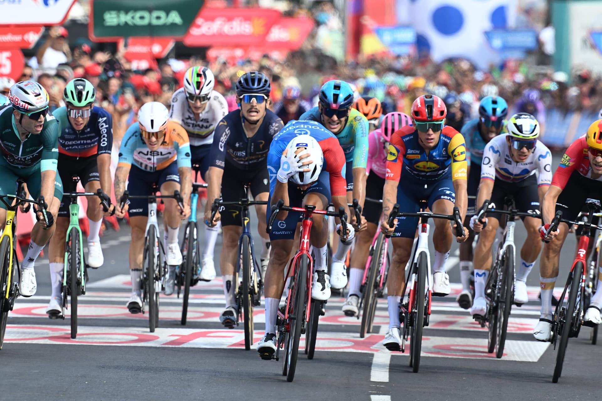 Bastien Tronchon, Wout van Aert en andere renners sprinten over de finish in een chaotische Vuelta-finale.