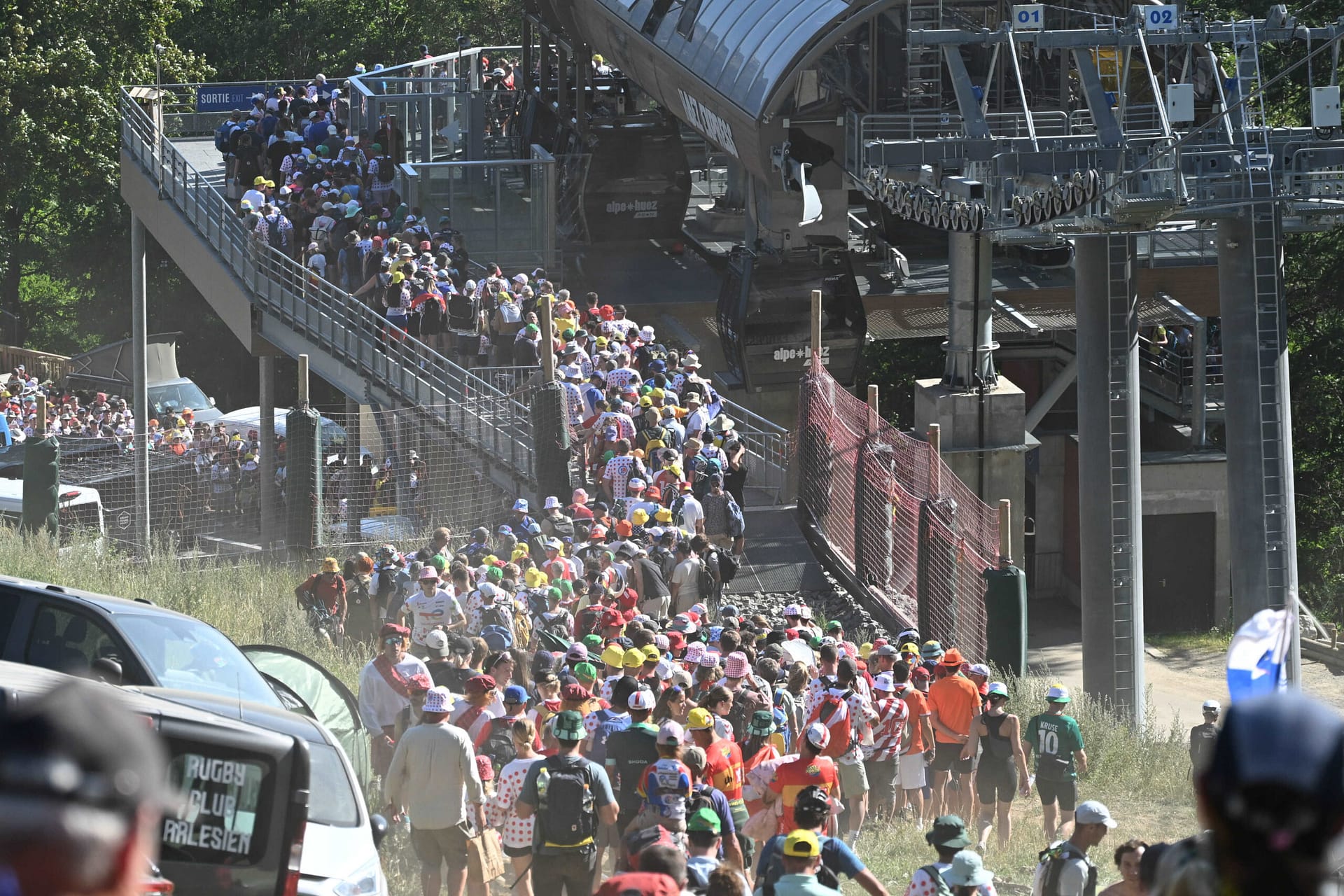 Wielerfans pack the roadside stands as cyclists race past near a stadium bridge on a hot day