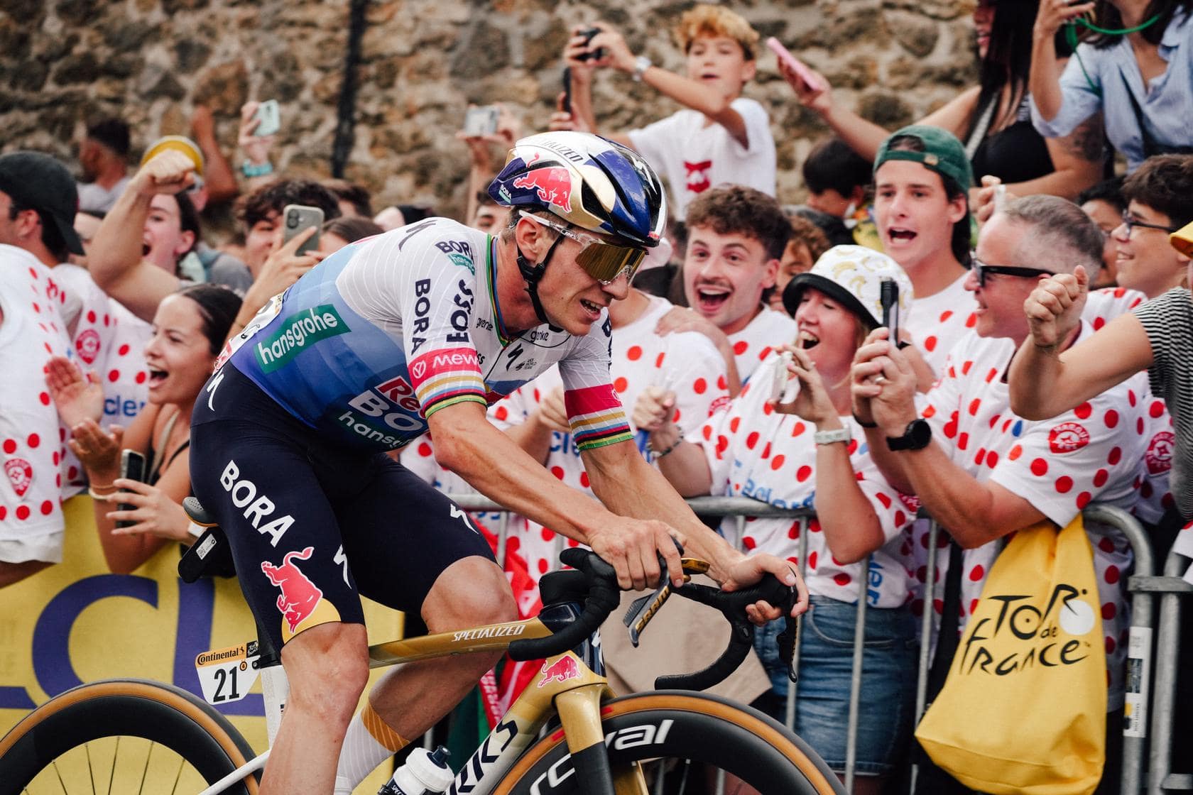 Cyclist in blue helmet leans into the crowd as fans cheer in colorful jerseys along the Tour route